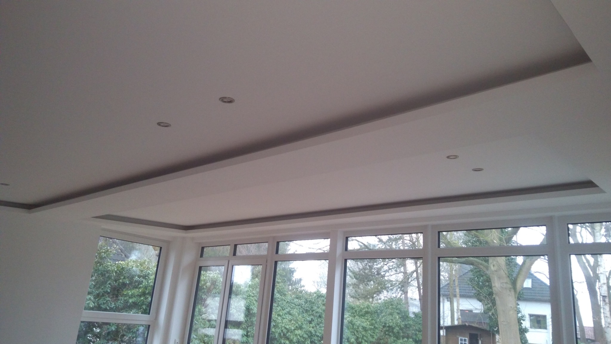 Nowoczesny sufit podwieszany z oświetleniem punktowym w nowym domu z dużymi oknami wychodzącymi na ogród.