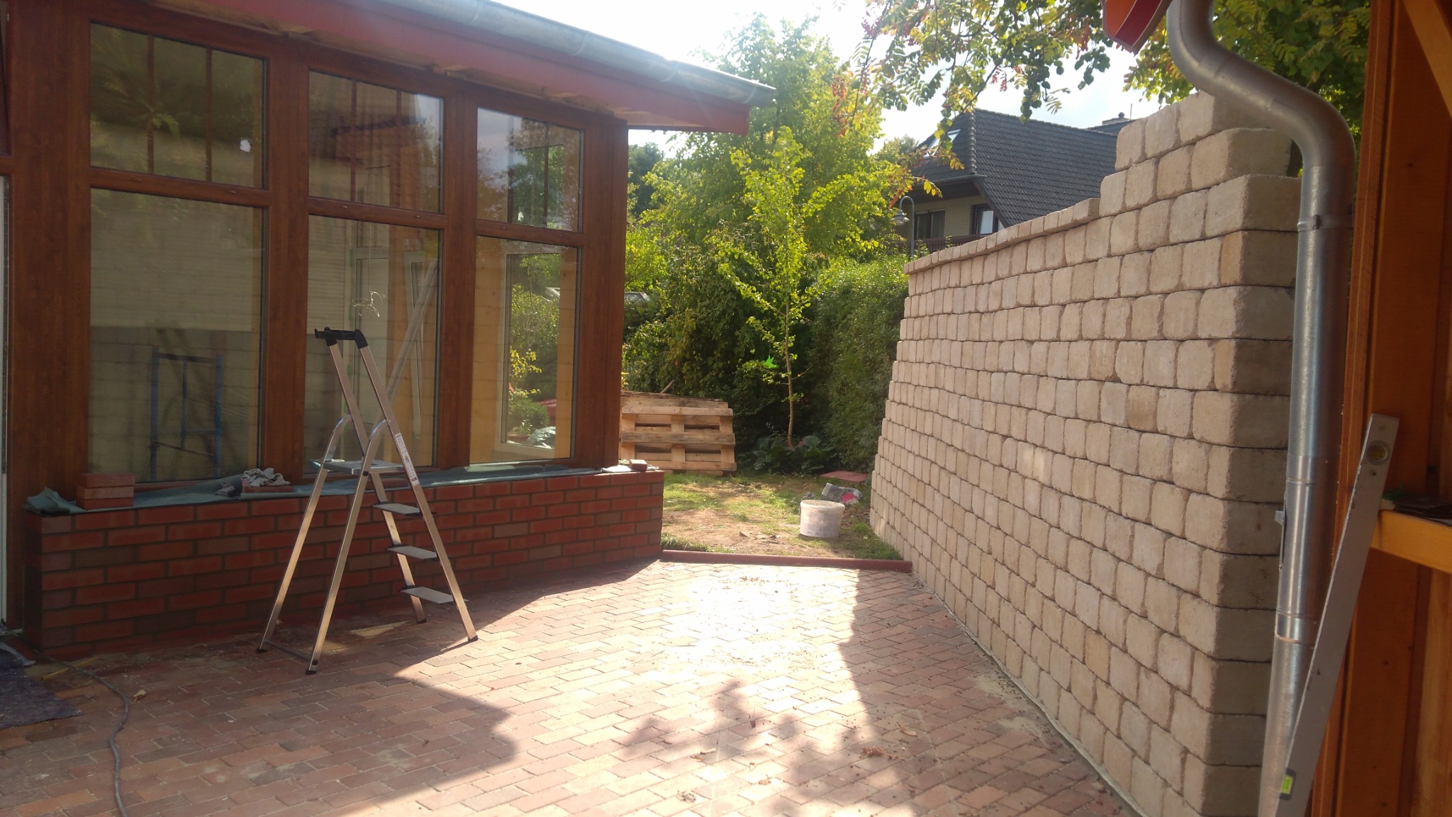 Ściana z bloczków betonowych w trakcie budowy, widoczna drabina oparta o okno i paleta w tle.