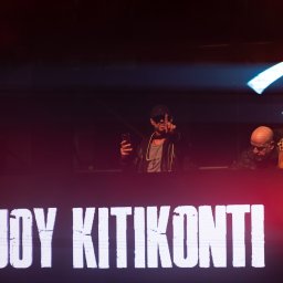 MARCIN FLAJSZER HANDEL I USŁUGI - Zdjęcie z koncertu w Wartowni Gorzów Wielkopolski. Na pierwszym planie napis 'JOY KITIKONTI', w tle DJ z telefonem i lampa w stylu retro.