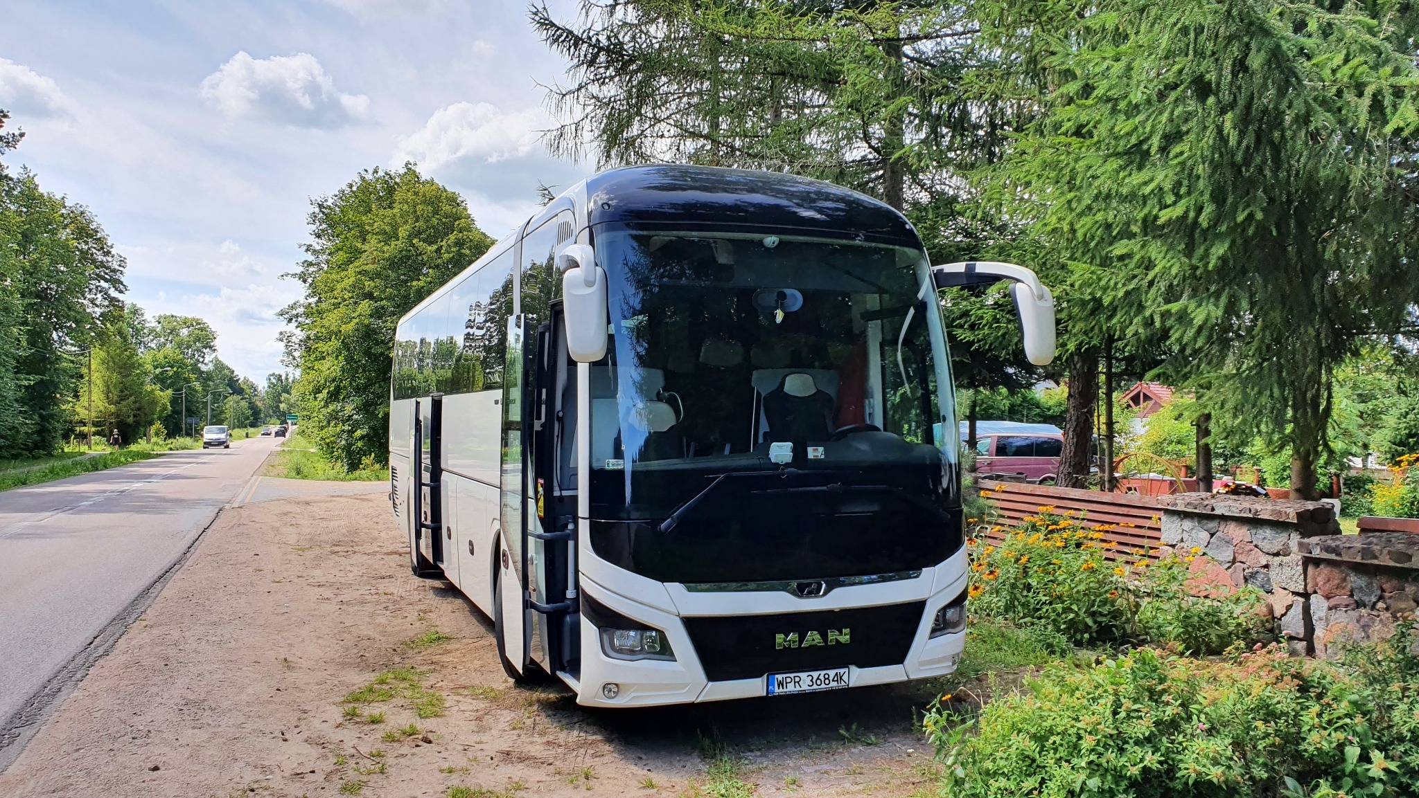 Biały autokar marki MAN zaparkowany na poboczu drogi w otoczeniu zieleni, widoczna tablica rejestracyjna WPR 3684K.