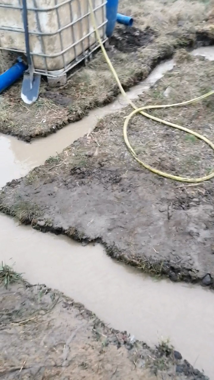 Wiercenie w gruncie, widoczne wykopane rowy wypełnione wodą, zbiornik na wodę i narzędzia. Żółty wąż na ziemi.