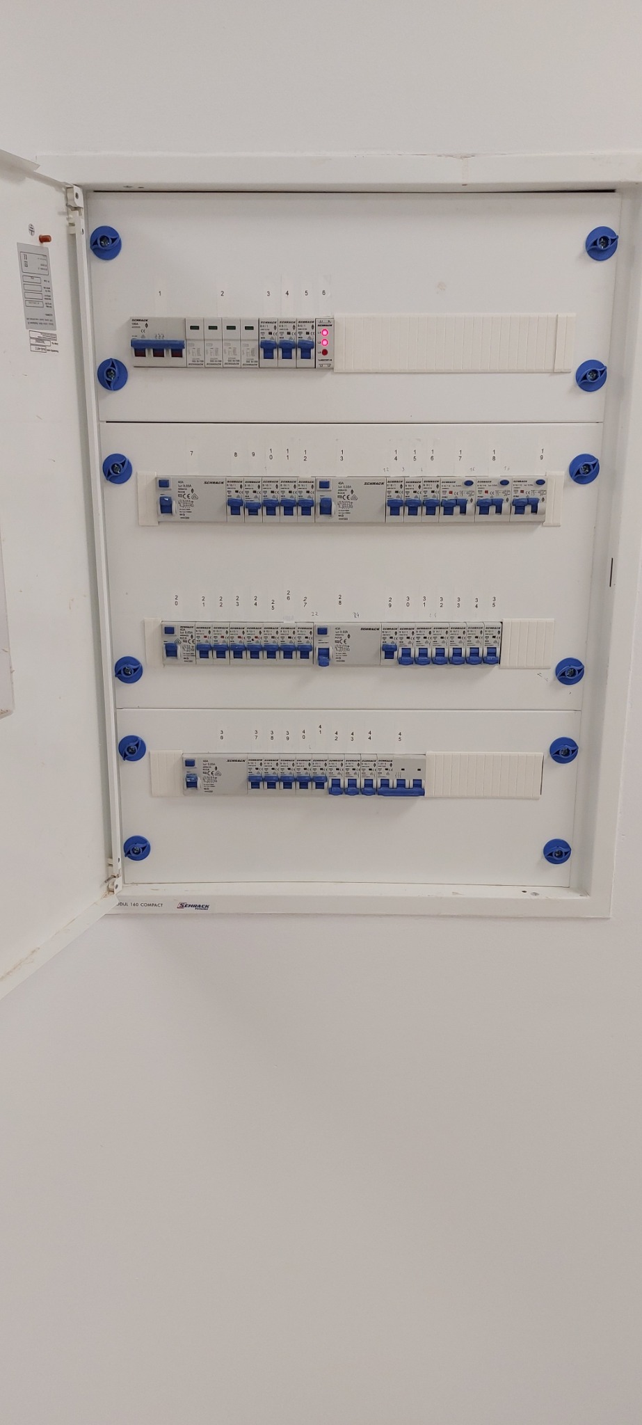 Otwarta skrzynka bezpiecznikowa Schrack z widocznymi bezpiecznikami i wyłącznikami różnicowoprądowymi, jeden z bezpieczników oznaczony czerwoną diodą LED.