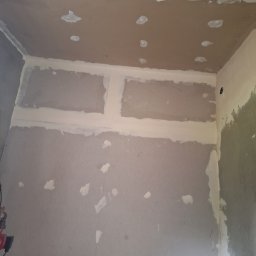 Bartosz Czerwiński - Wnętrze w trakcie prac przygotowawczych do wykończenia, widoczne płyty gipsowo-kartonowe z zaszpachlowanymi łączeniami i otworami, sufit w trakcie obróbki.