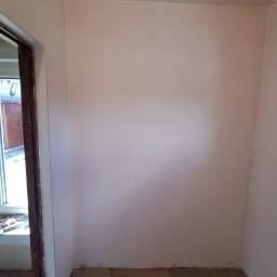 Bartosz Czerwiński - Pomalowane na jasny kolor ściany w rogu pomieszczenia z widoczną podłogą z płytek i fragmentem okna z narzędziami.