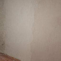 Bartosz Czerwiński - Ściana w trakcie prac przygotowawczych, częściowo pokryta gładzią, widoczny wąż od odkurzacza i zabrudzona podłoga z paneli.