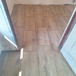 Bartosz Czerwiński - Ułożone panele podłogowe imitujące drewno, widoczne niedoskonałości wykończenia przy ościeżnicy drzwi.