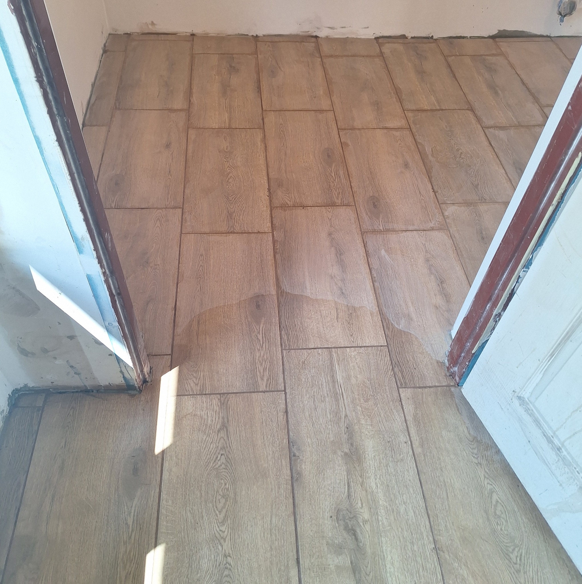 Ułożone panele podłogowe imitujące drewno, widoczne niedoskonałości wykończenia przy ościeżnicy drzwi.