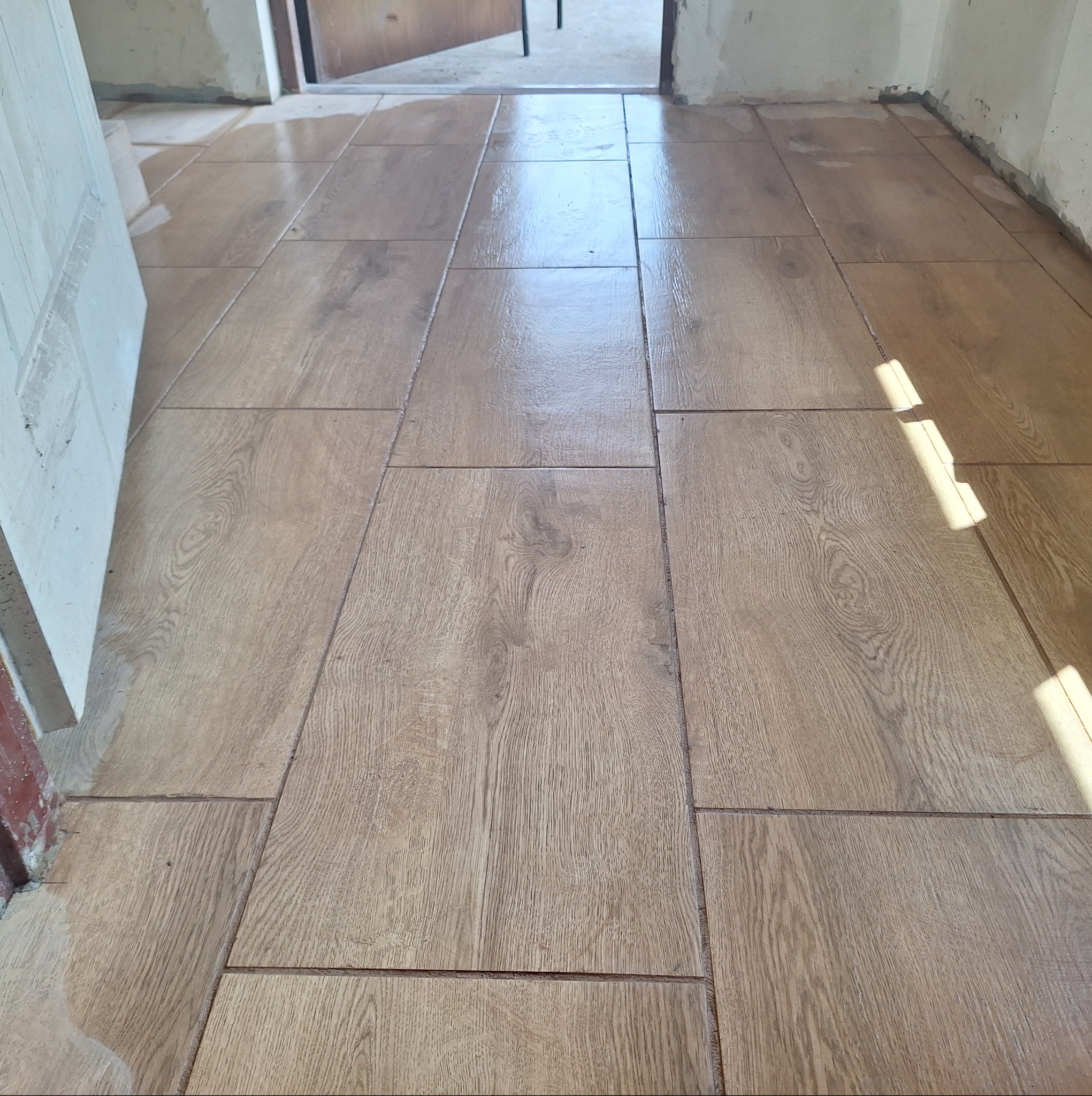 Ułożone płytki podłogowe imitujące drewno, z widocznymi śladami świeżego fugowania i resztkami zaprawy na ścianach.