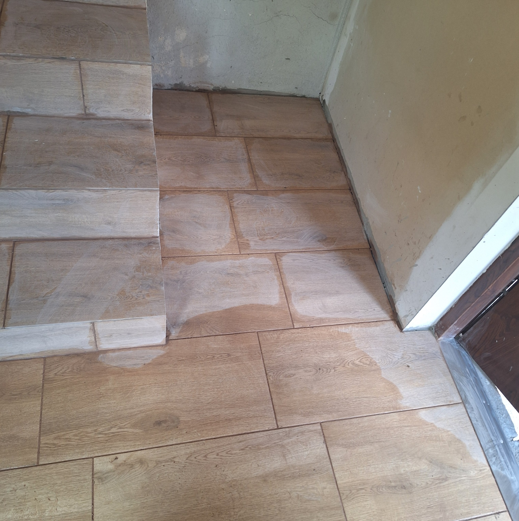 Ułożona podłoga z płytek imitujących drewno, częściowo zabrudzona pozostałościami po fugowaniu, widoczne surowe ściany w trakcie prac wykończeniowych.