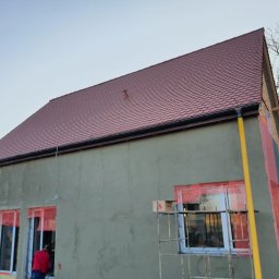 Polskiedachy - Budynek w Bydgoszczy z nowym, czerwonym dachem z dachówki, szarą elewacją w trakcie ocieplania, widoczne okna zabezpieczone folią i rusztowanie.