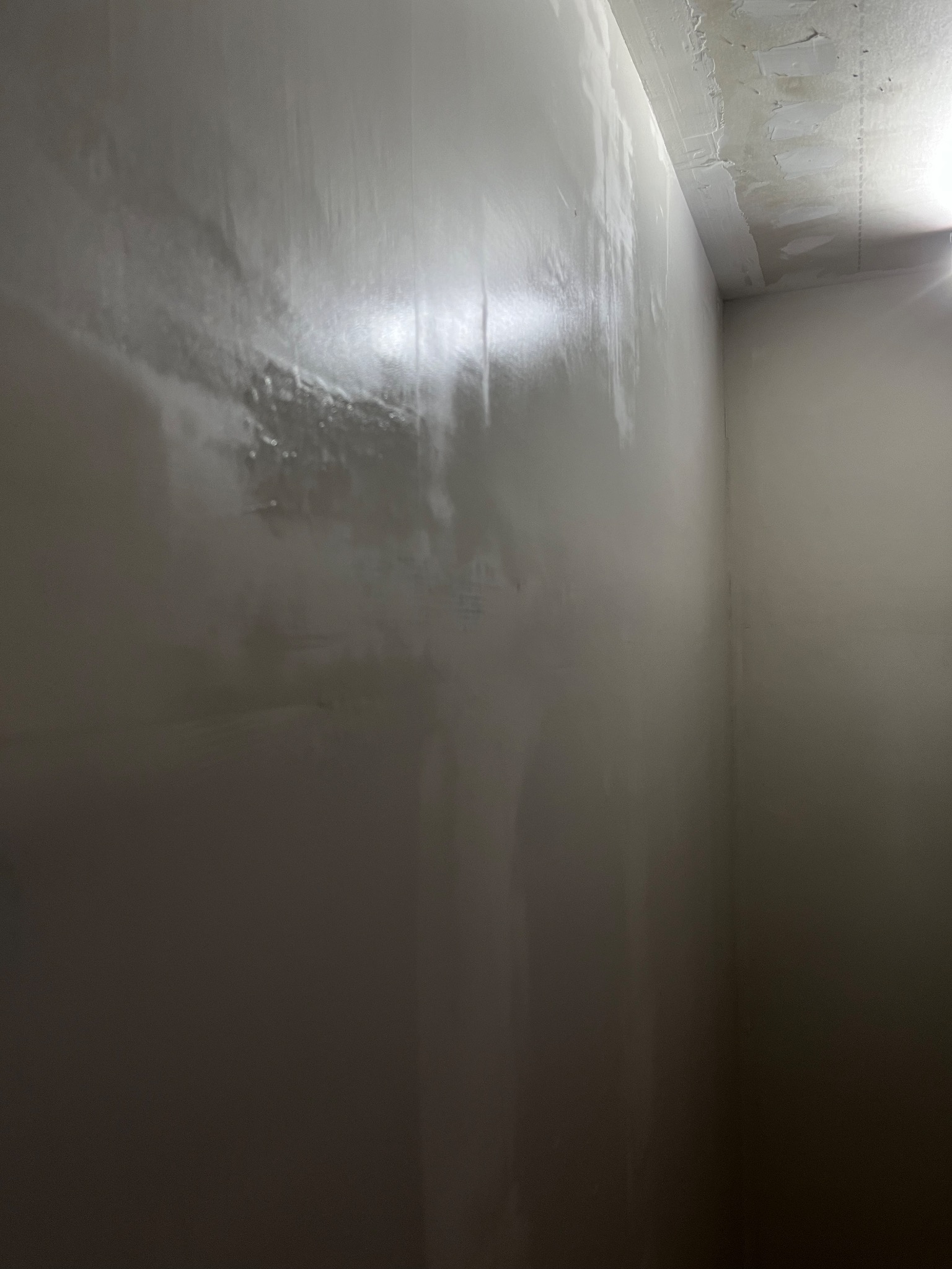 Ściana w rogu pomieszczenia po nałożeniu gładzi, widoczne ślady po szpachlowaniu na ścianie i suficie, przygotowanie do malowania.