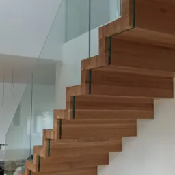 Nowoczesne, drewniane schody samonośne z balustradą ze szkła hartowanego, widoczne z boku, z minimalistycznym wykończeniem wnętrza.