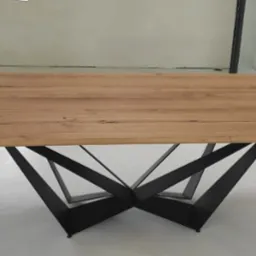 Stół z blatem z jasnego drewna i geometryczną podstawą z czarnych metalowych elementów