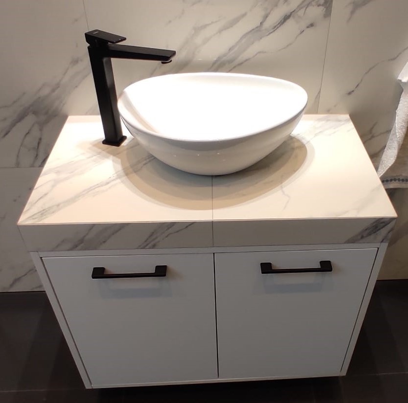 Nowoczesna łazienka: biała umywalka nablatowa w kształcie misy z czarną armaturą, szafka pod umywalkę z białymi frontami i marmurowym blatem.