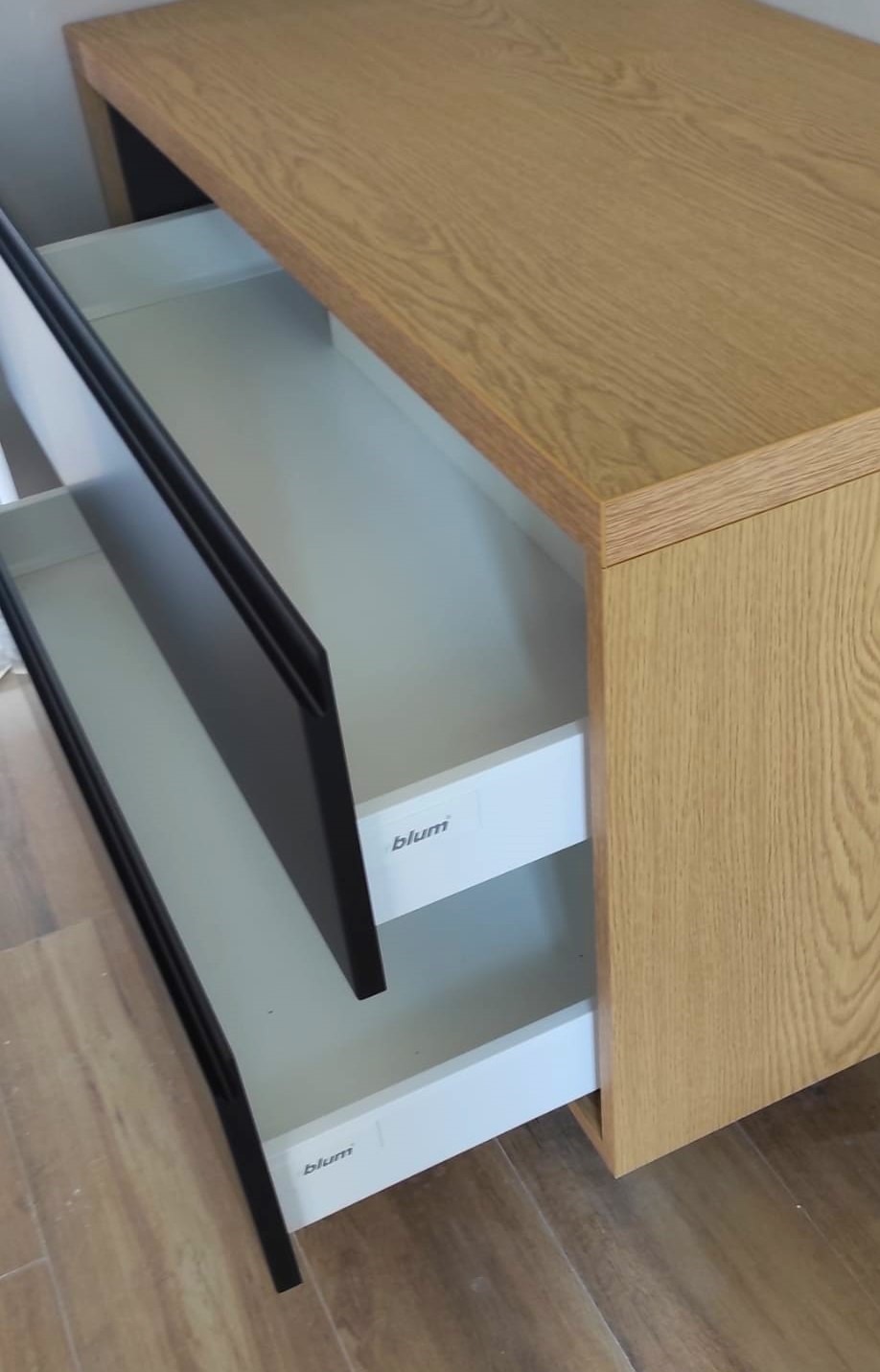 Otwarta szuflada w komodzie z jasnego drewna, widoczne okucia firmy Blum.
