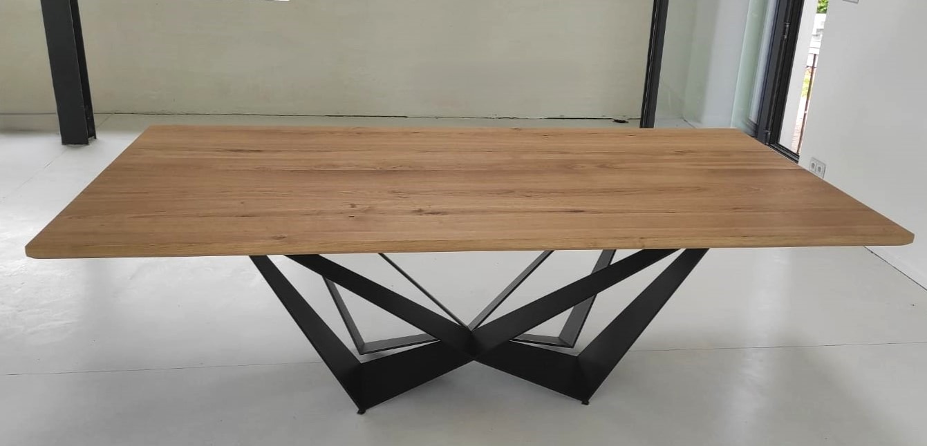 Stół z blatem z jasnego drewna i geometryczną podstawą z czarnych metalowych elementów