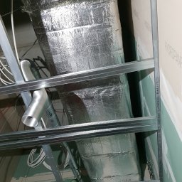 A&W SERVICE Wiesław Iwanowski - Kanciasty kanał wentylacyjny owinięty folią aluminiową, zamontowany pod sufitem z metalową konstrukcją i płytami gipsowo-kartonowymi, widoczne przewody i elastyczny przewód wentylacyjny.