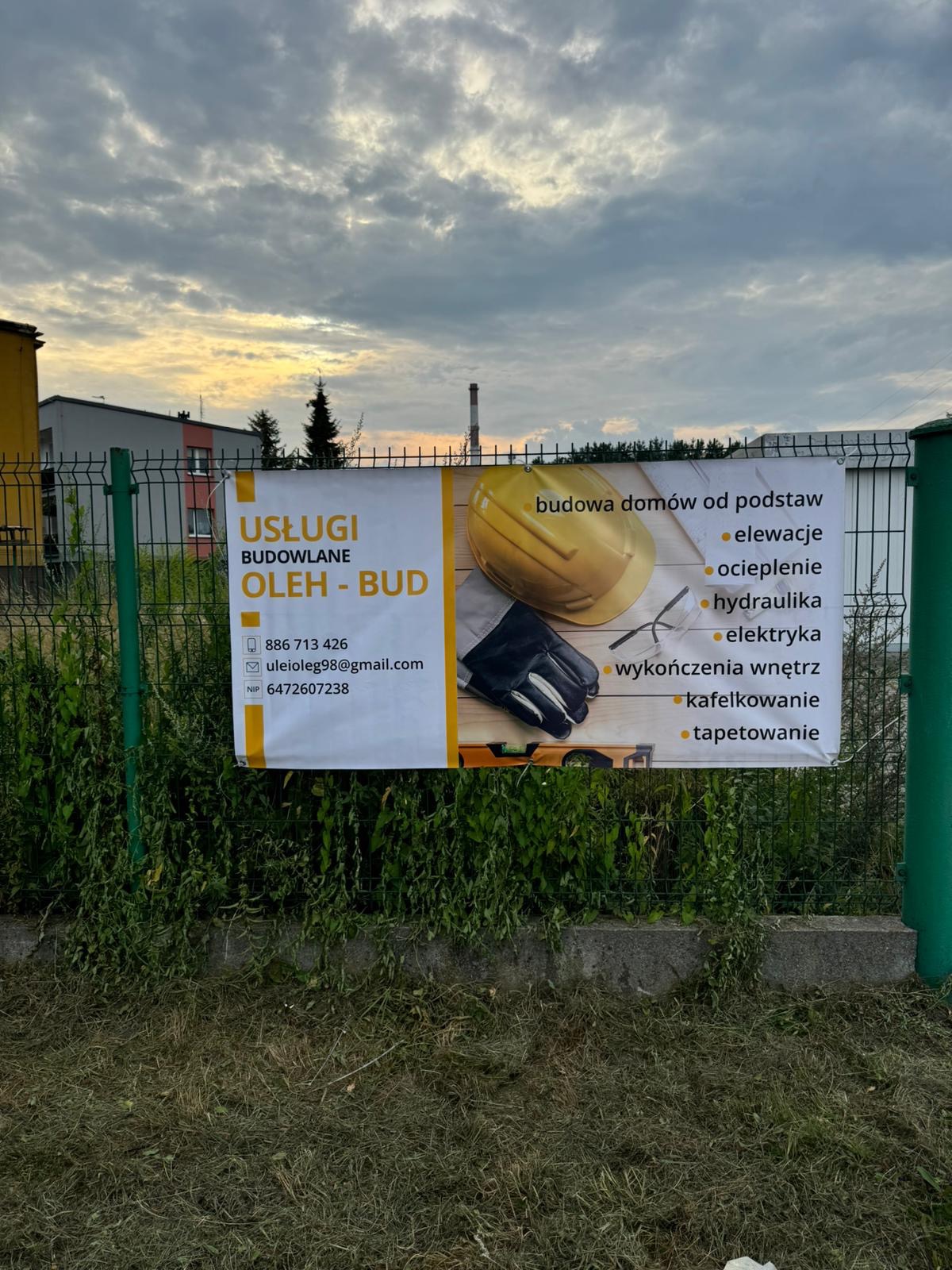 Baner reklamowy usług budowlanych firmy Oleh-Bud, zawieszony na ogrodzeniu, z widocznymi danymi kontaktowymi i listą oferowanych prac: budowa domów, elewacje, ocieplenie, hydraulika, elektryka...