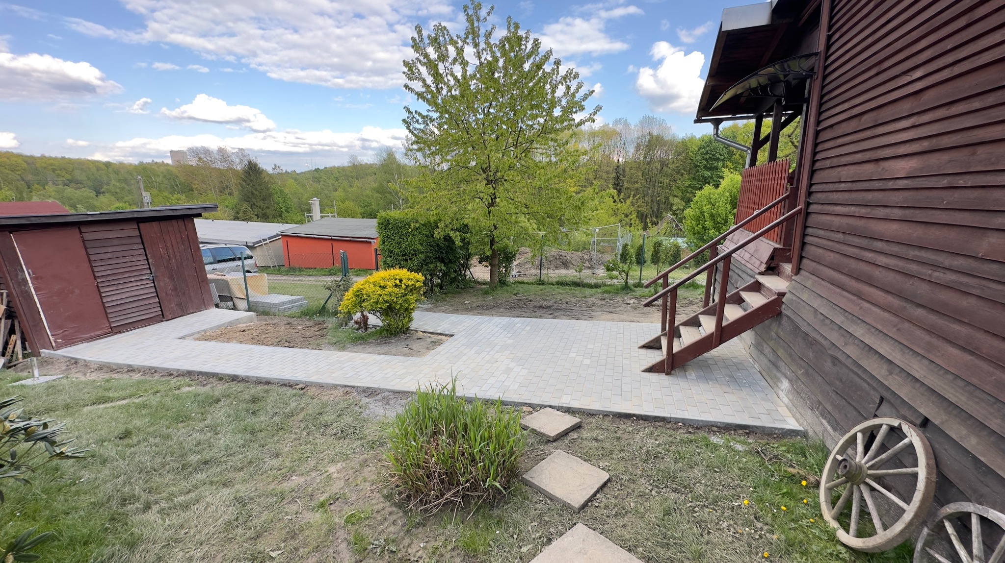 Nowa, jasna kostka brukowa ułożona jako ścieżka wokół drewnianego domu w Wodzisławiu Śląskim, prowadząca od schodów wejściowych do budynku gospodarczego, z widocznymi elementami dekoracyjnymi jak...