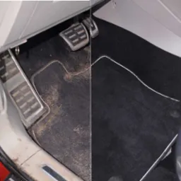 Dywanik samochodowy: porównanie stanu przed i po czyszczeniu. Po lewej stronie widoczny mocno zabrudzony dywanik w okolicach pedałów, po prawej - czysty, czarny dywanik z białą lamówką.