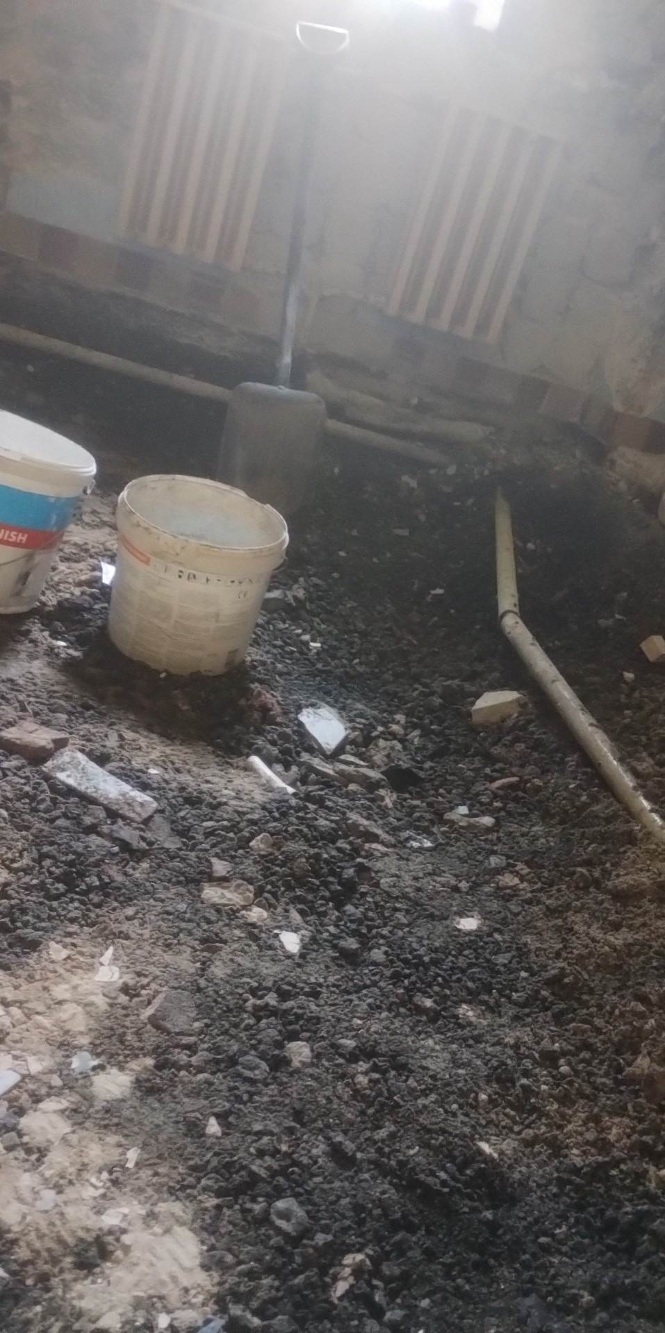 Wnętrze pomieszczenia w trakcie prac wyburzeniowych, widoczne gruz, rury i puste wiadra po farbie.