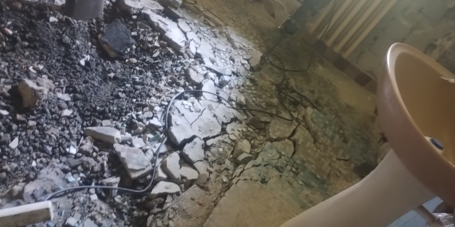 Gruz i resztki zdemontowanej ściany z widoczną instalacją elektryczną oraz fragmentem umywalki w rogu.