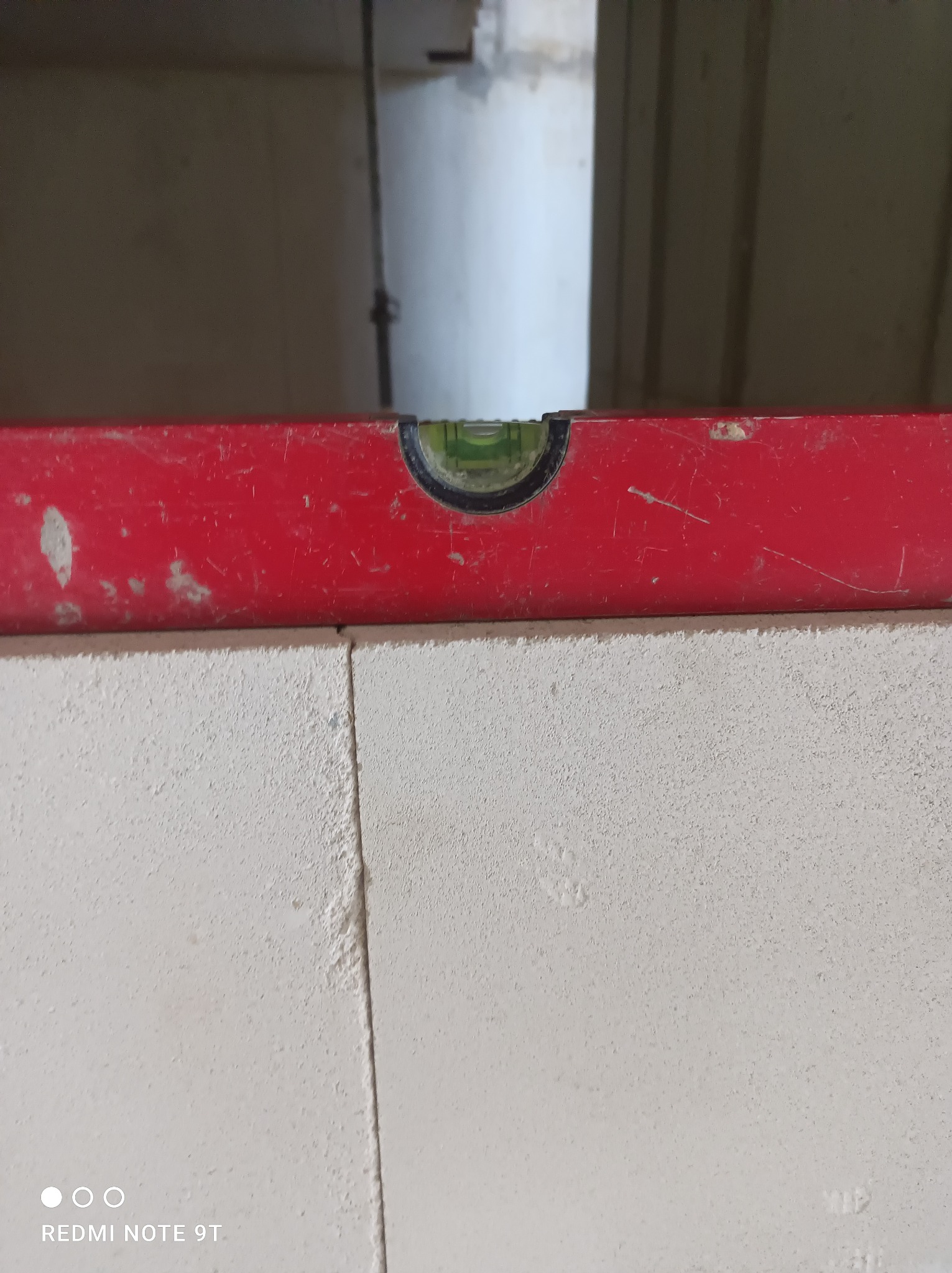 Czerwona poziomica spoczywa na bloczkach z betonu komórkowego, sprawdzając ich wypoziomowanie podczas budowy ściany w surowym stanie.