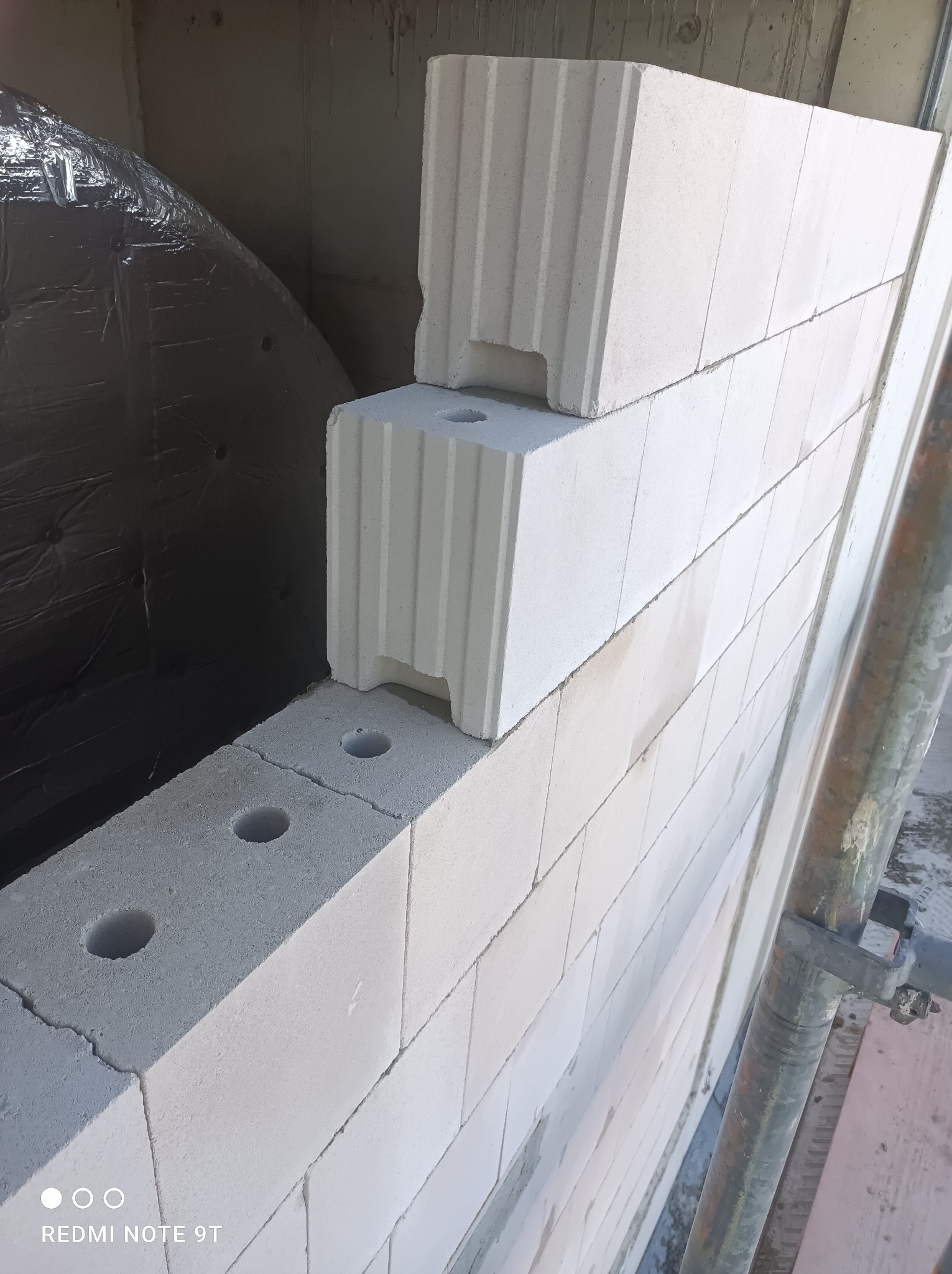 Wznoszenie ściany z bloczków betonu komórkowego Ytong z widoczną izolacją przeciwwilgociową za ścianą, częściowo ułożone bloczki z otworami na zaprawę.