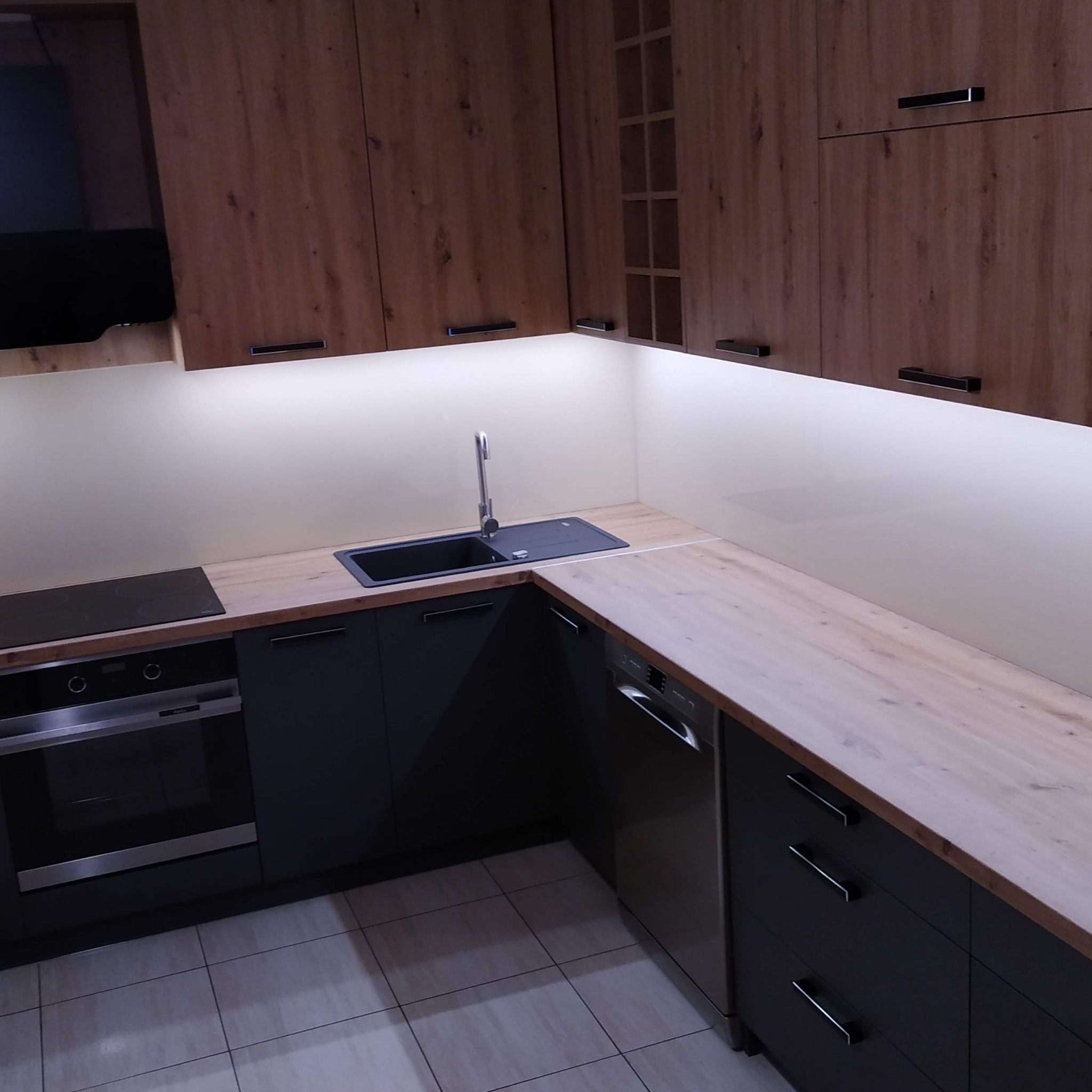 Nowoczesna kuchnia w odcieniach brązu i grafitu z drewnianym blatem, oświetleniem LED pod szafkami i czarnym zlewozmywakiem.