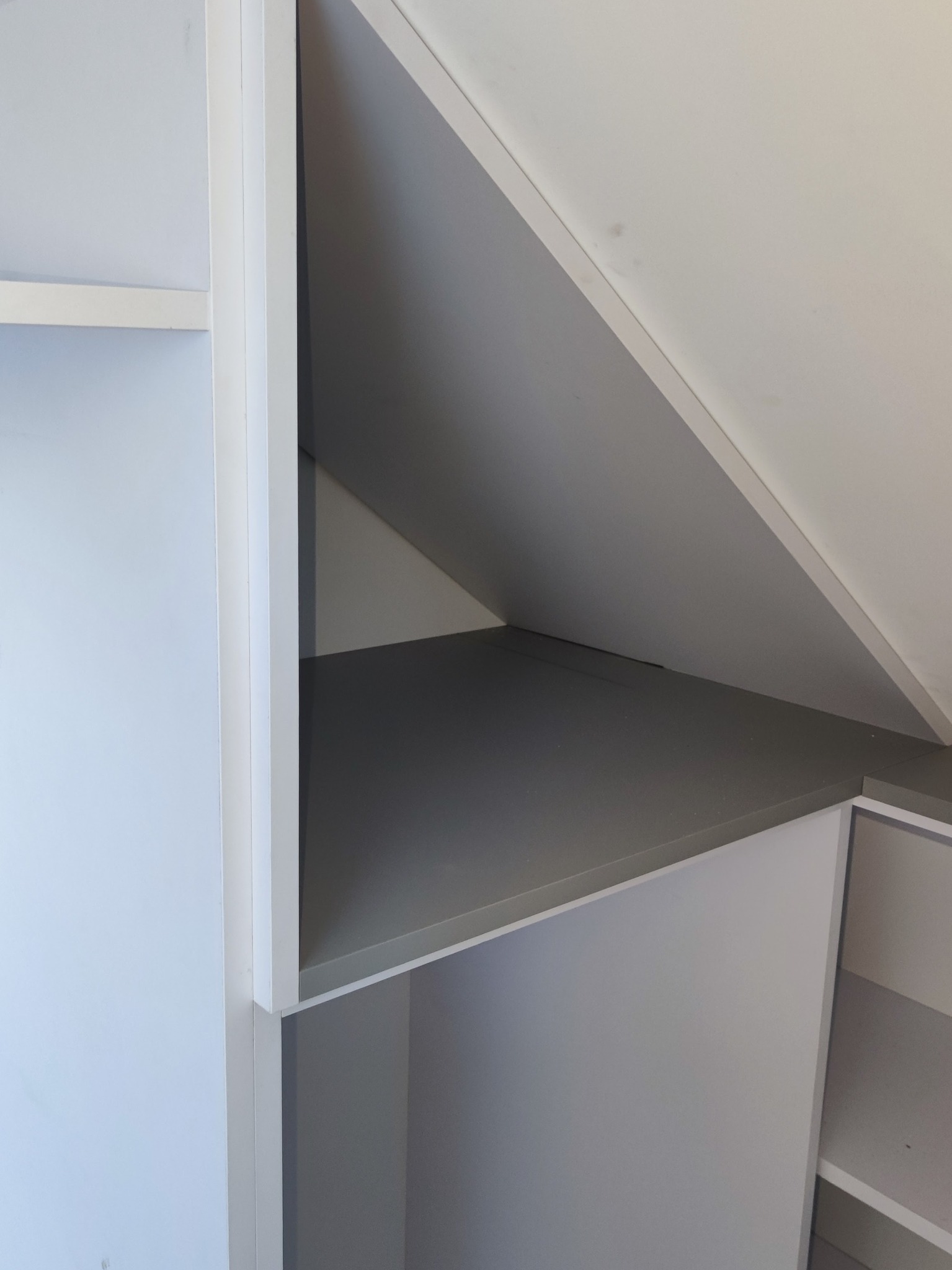 Biało-szara zabudowa wnęki pod skosem dachu z półkami, widok z bliska na detale konstrukcyjne.