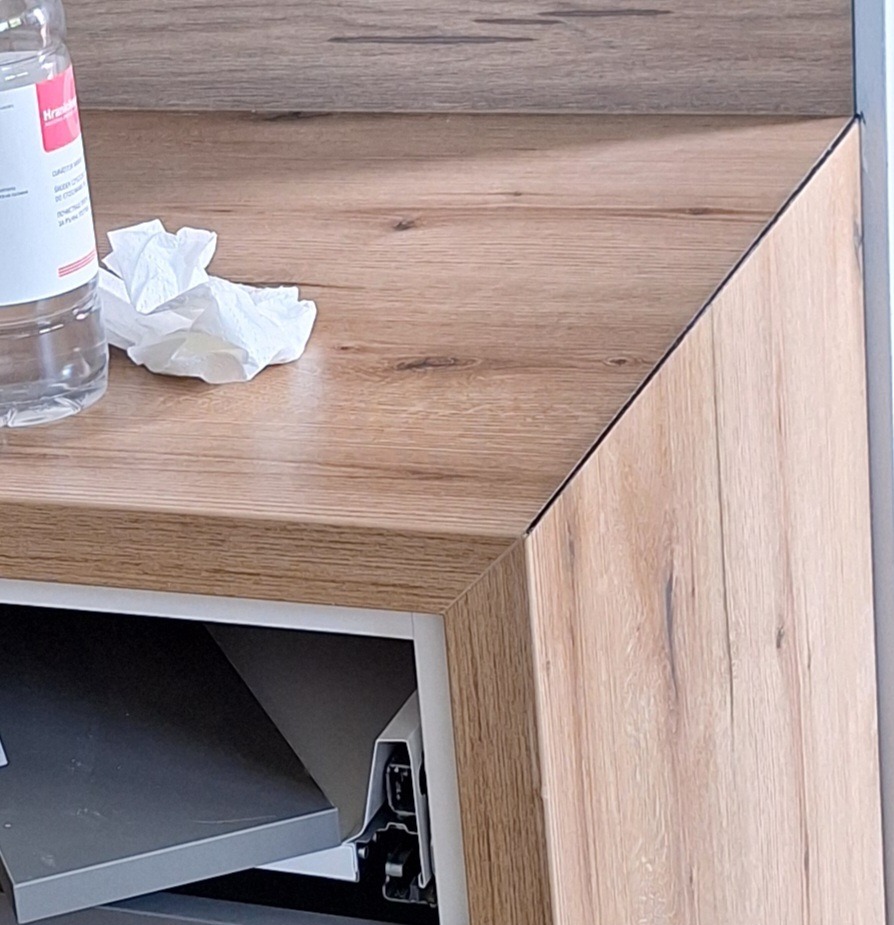 Fragment szafki z drewnopodobnym blatem, otwartą szufladą i butelką płynu oraz zmiętą chusteczką na blacie.
