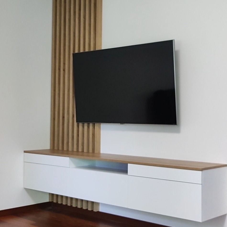 Nowoczesna szafka RTV z białymi frontami i drewnianym blatem, zintegrowana z dekoracyjną ścianką z pionowych drewnianych listew, pod wiszącym telewizorem.