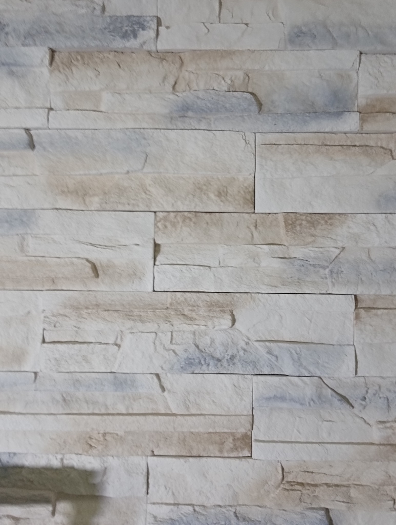 Dekoracyjna ściana z jasnych, nieregularnych kamieni imitujących piaskowiec, ułożonych w poziome pasy. Widoczne subtelne odcienie beżu i szarości.