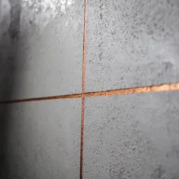 Szare płytki ścienne z miedzianymi fugami, zbliżenie na skrzyżowanie fug, nowoczesny design, oświetlenie z lewej strony.