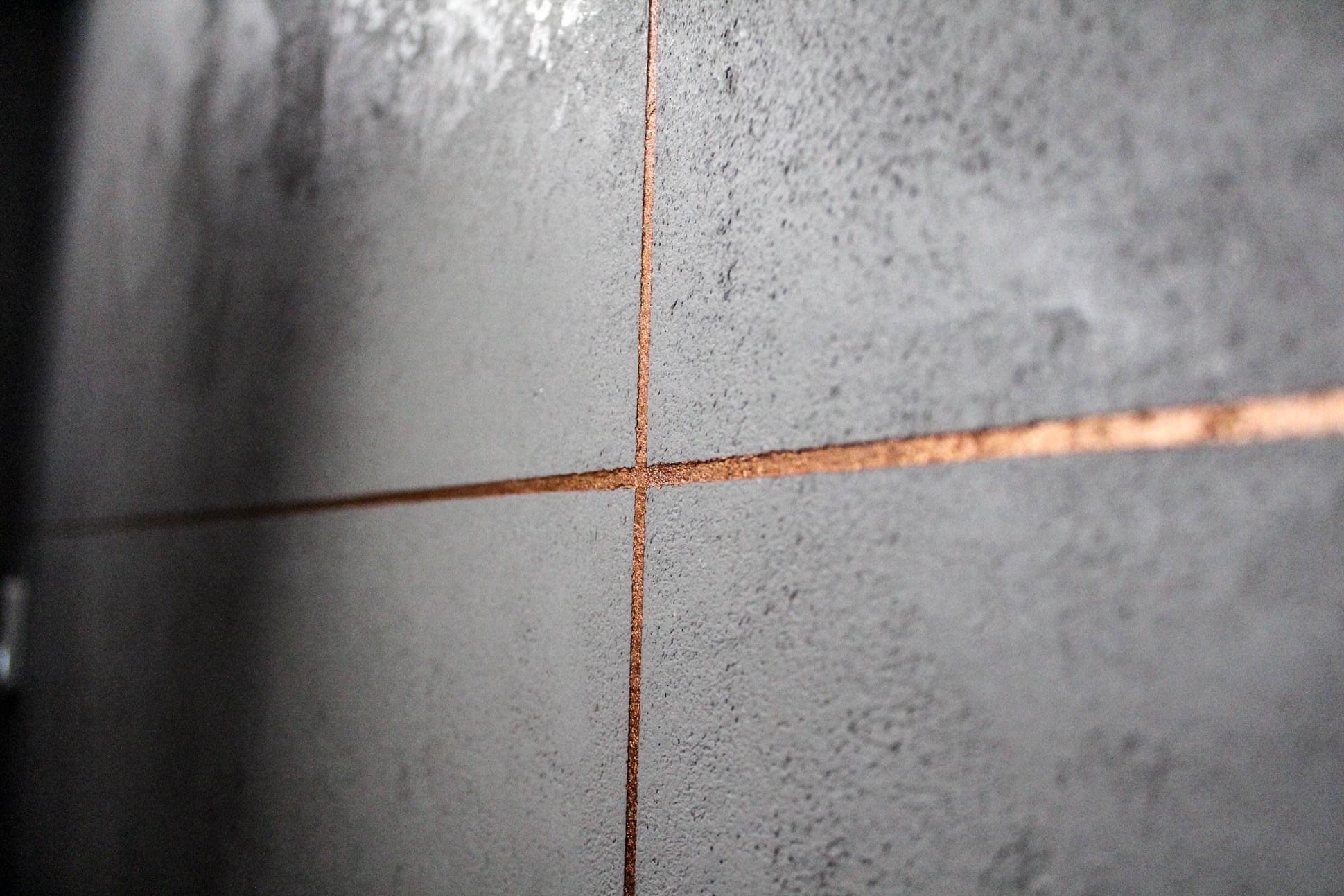 Szare płytki ścienne z miedzianymi fugami, zbliżenie na skrzyżowanie fug, nowoczesny design, oświetlenie z lewej strony.