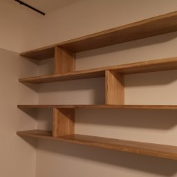 Woodland - Asymetryczne, wiszące półki z jasnego drewna w minimalistycznym wnętrzu, mocowane do ściany, z widocznymi naturalnymi słojami drewna i subtelnym oświetleniem.