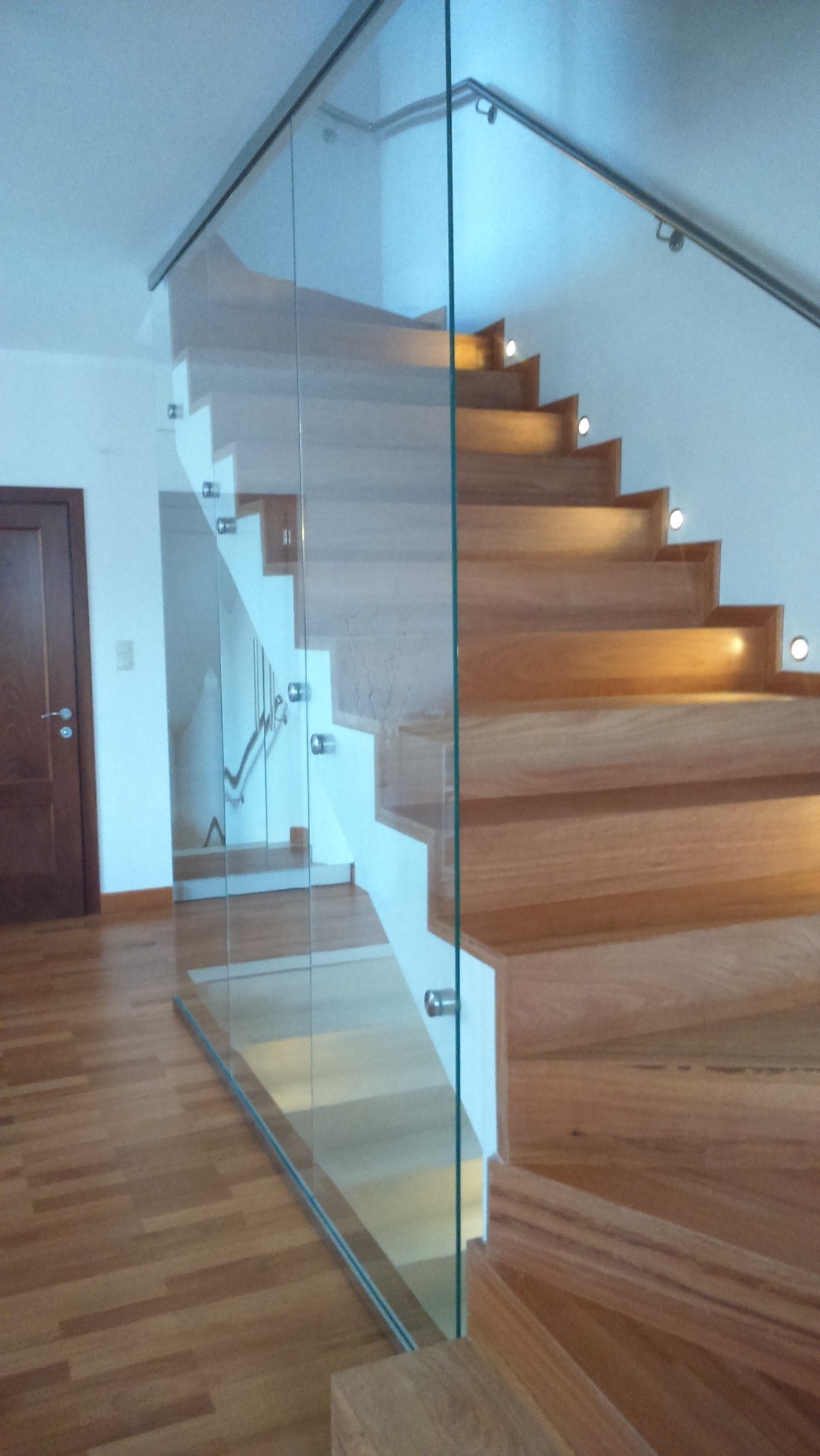 Nowoczesne schody z drewna i szkła, z podświetleniem LED na każdym stopniu, widok z dołu, parkiet na podłodze, minimalistyczny design.