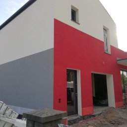 Remont Yaroslav Mazur - Nowo otynkowany dom z trzema kolorami elewacji: szarym u dołu, czerwonym pośrodku i białym u góry. Widoczne okna z folią ochronną i drzwi wejściowe z czarną ramą.