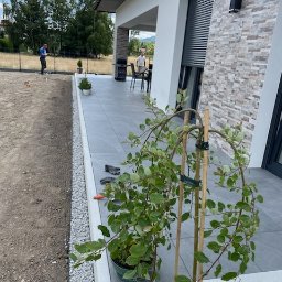 Remont Yaroslav Mazur - Nowoczesny taras z szarych płyt, obrzeże z białego grysu, trawnik w trakcie zakładania, widoczny człowiek z niwelatorem w tle.