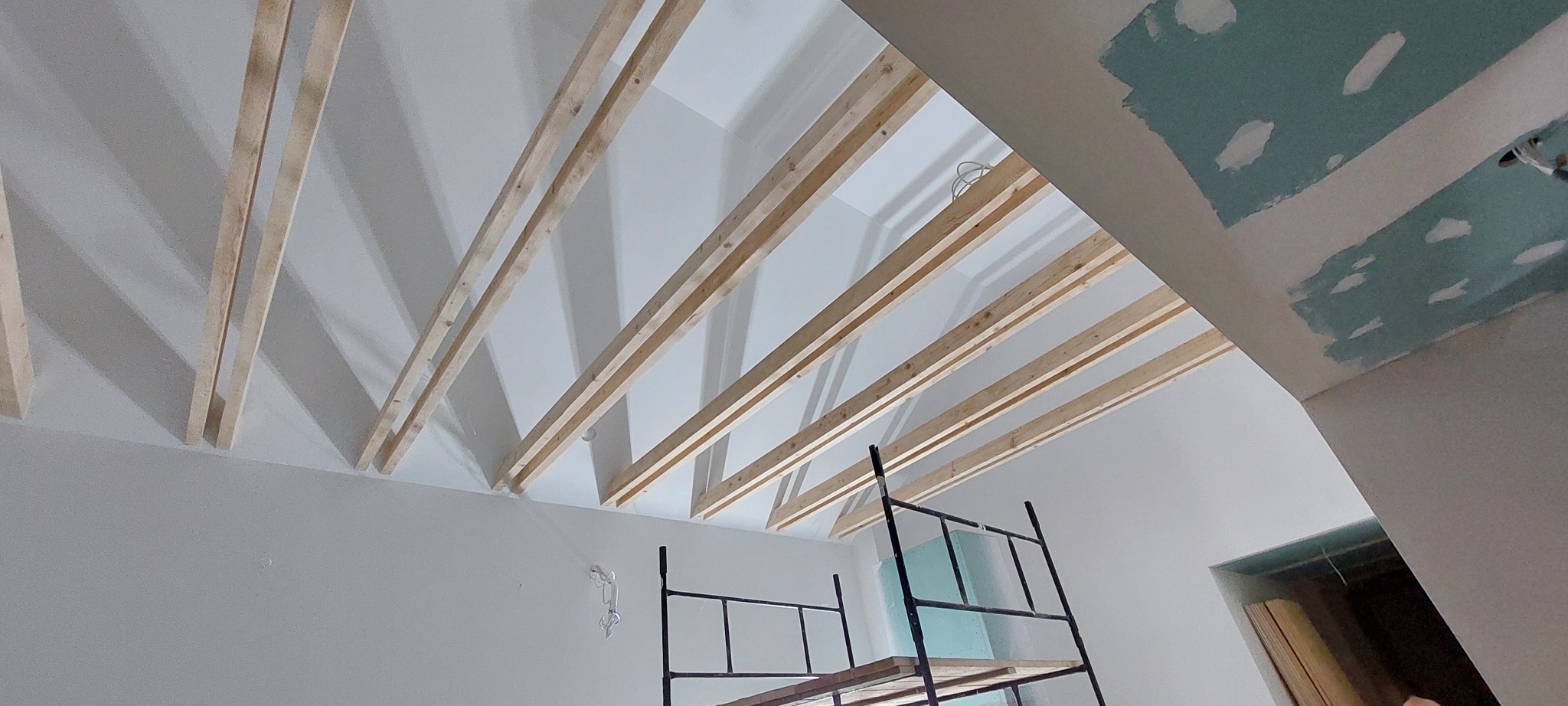 Drewniana konstrukcja sufitu podwieszanego, widok z dołu, w tle fragment rusztowania i ściana z widocznymi śladami szpachlowania.