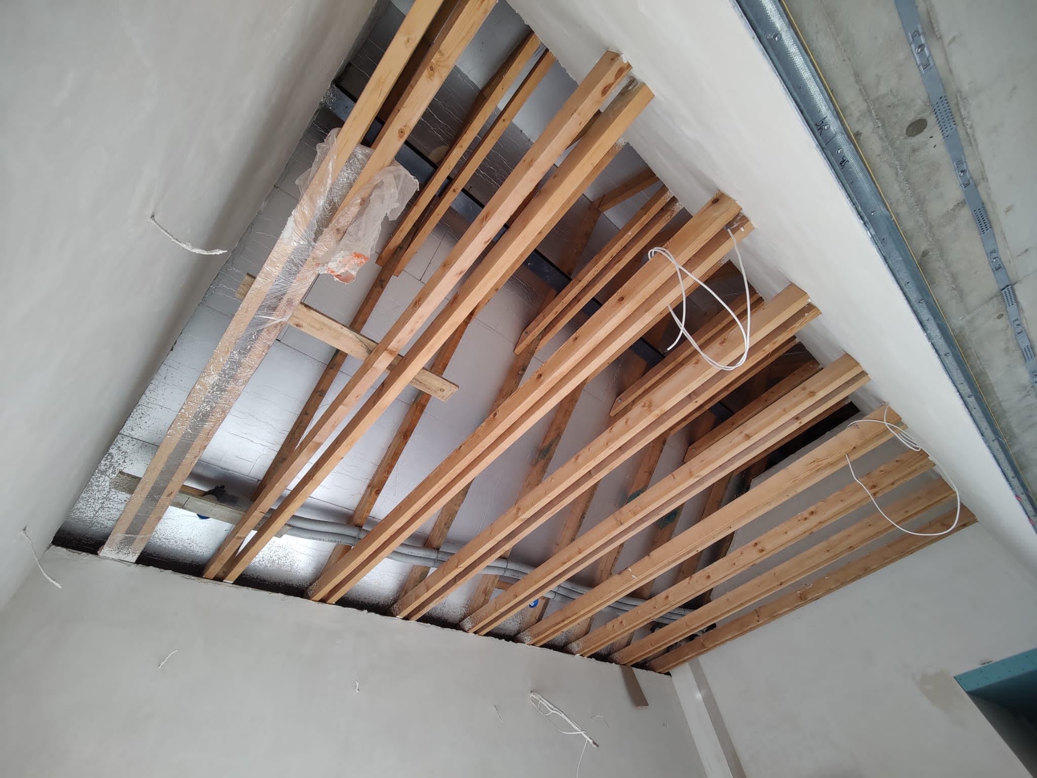 Konstrukcja drewniana poddasza z izolacją, widok z dołu w Bielsko-Białej. Elementy metalowe na suficie, przewody elektryczne. Prace wykończeniowe w trakcie.