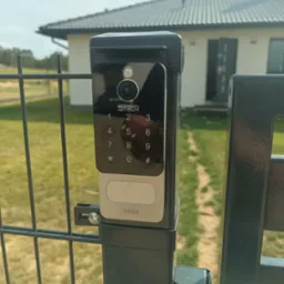 Nowoczesny wideodomofon firmy Stech zamontowany na metalowym ogrodzeniu panelowym w Gubinie, z widocznym panelem dotykowym i kamerą, na tle domu jednorodzinnego.