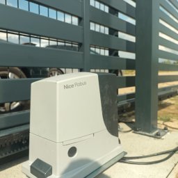 ARTELMET - Szara, nowoczesna brama wjazdowa z automatyką Nice Robus; widoczny fragment samochodu po drugiej stronie bramy.