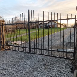 ARTELMET - Automatyczna brama wjazdowa z pionowych prętów w Gubinie, widoczny napęd i żwirowe podłoże.