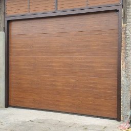 ARTELMET - Zewnętrzna brama garażowa segmentowa w kolorze drewna z poziomymi panelami, zamontowana w budynku z szarą dachówką i elementami ceglanymi.