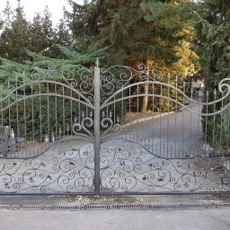 ARTELMET - Otwarta, metalowa brama wjazdowa z ozdobnymi, kutymi elementami na tle zielonych drzew i krzewów; widoczny fragment napędu i mężczyzna w czarnej koszulce.