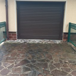 ARTELMET - Brązowa brama rolowana garażowa, zielone metalowe ogrodzenie z dwoma skrzydłami bramki, kamienny podjazd na posesji.