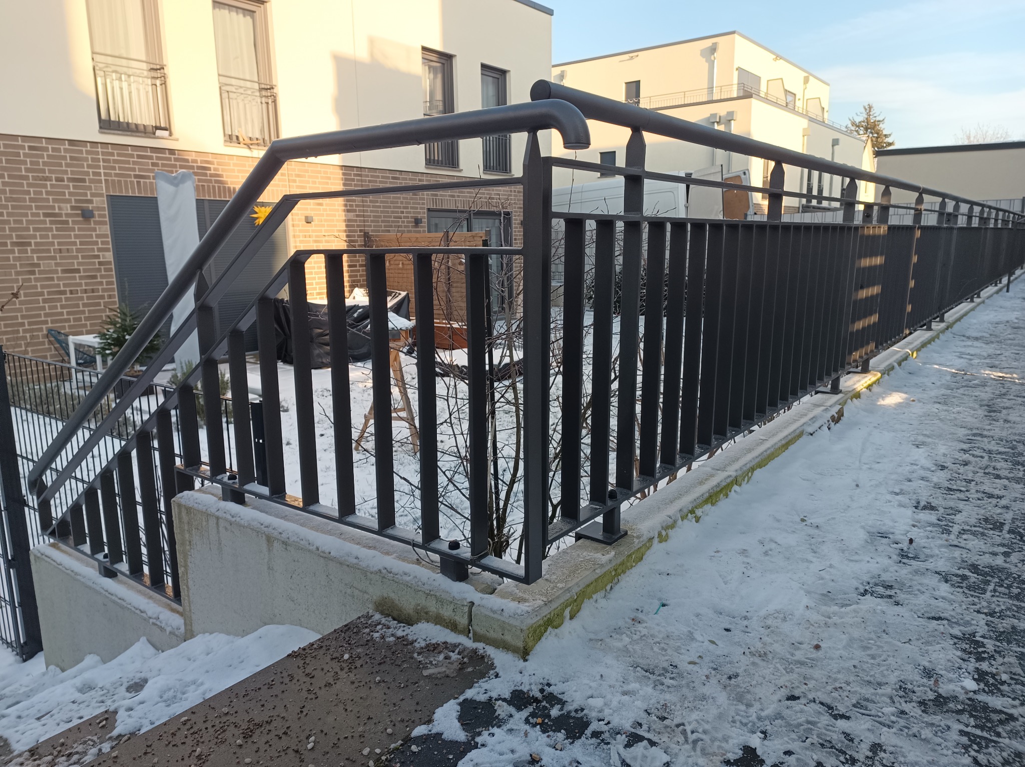 Ciemna, metalowa balustrada schodowa i balkonowa na tle nowoczesnego budynku mieszkalnego w zimowej scenerii.