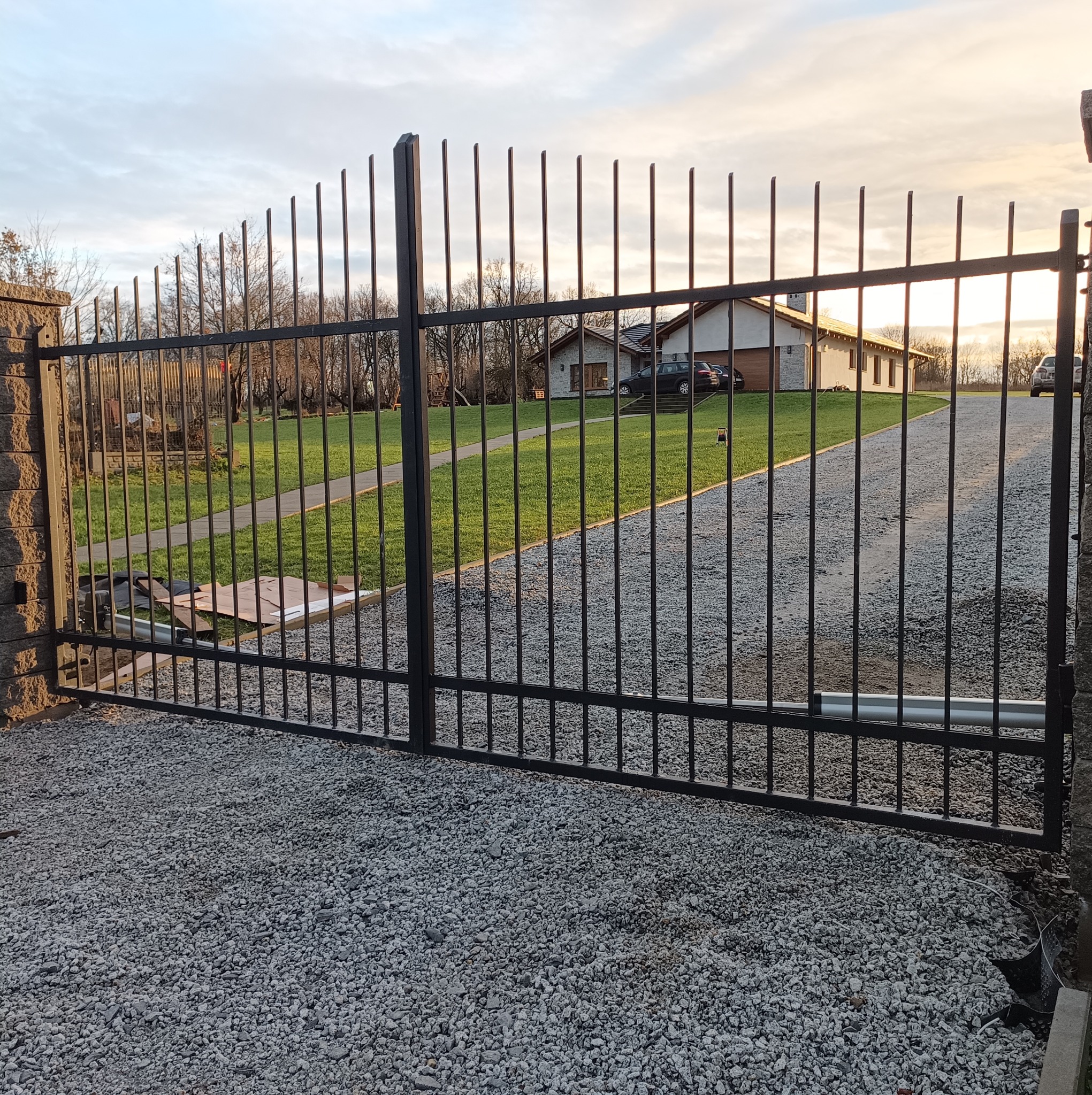 Automatyczna brama wjazdowa z pionowych prętów w Gubinie, widoczny napęd i żwirowe podłoże.