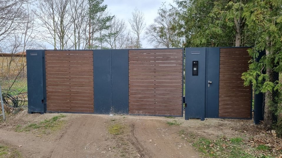 Nowoczesna brama wjazdowa z drewnopodobnymi panelami poziomymi i szarą metalową ramą, zintegrowany wideodomofon na furtce, widok z zewnątrz na podjazd.